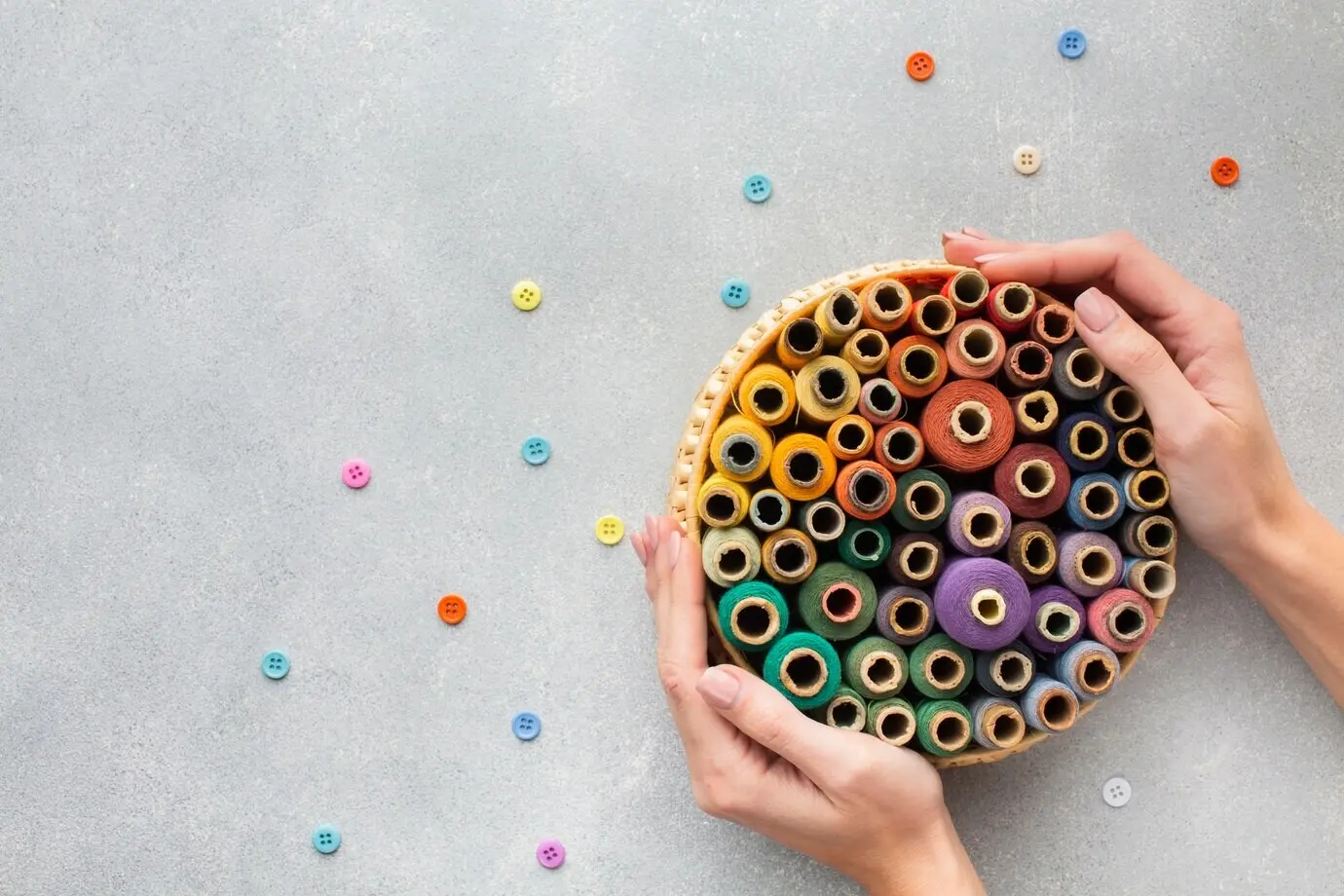 Draufsicht auf Hände, die einen Korb mit Nähgarnen halten.